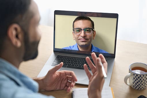 Latin indian businessman having virtual team meeting group call chatting with diverse people in customer support. Video conference call on computer with manager and employees.Â  Over shoulder view.